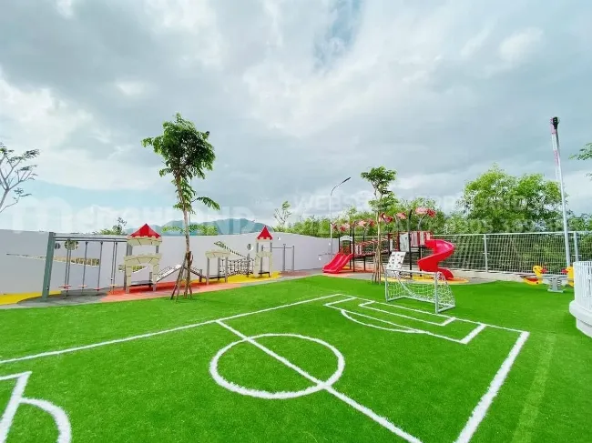 Khu vui chơi ngoài trời của trường mầm non trong dự án, có cầu trượt, xích đu trên nền cỏ nhân tạo an toàn, xung quanh là cây xanh